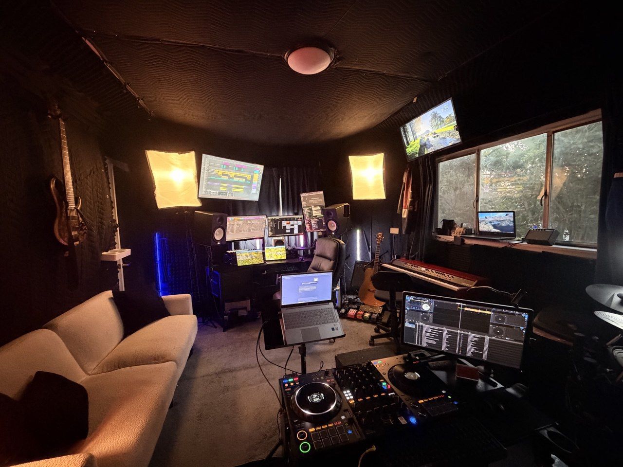 Studio wide shot with couch, DJ controller, multi-monitor DAW setup, and softbox lights