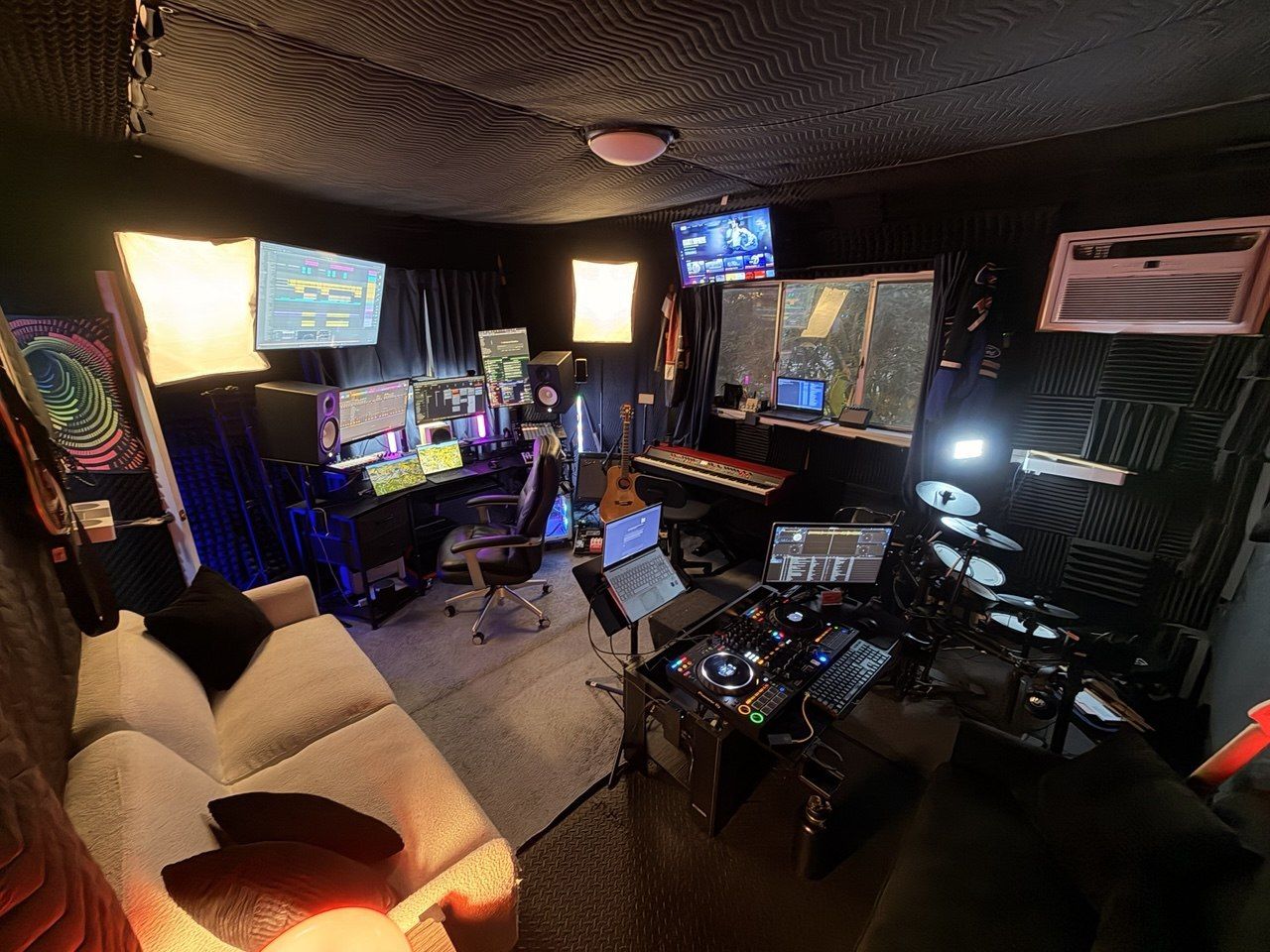 Full studio panorama with couch, DJ deck, drums, DAW screens, and colorful art